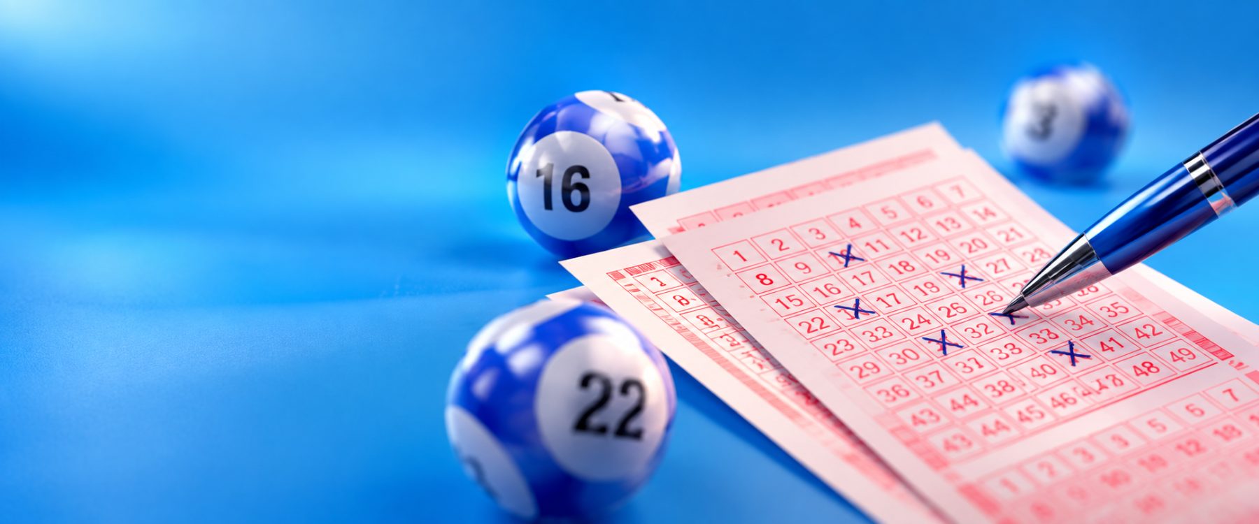 Vyplněný loterijní tiket s křížky, pero a modré loterijní koule s čísly 16 a 22